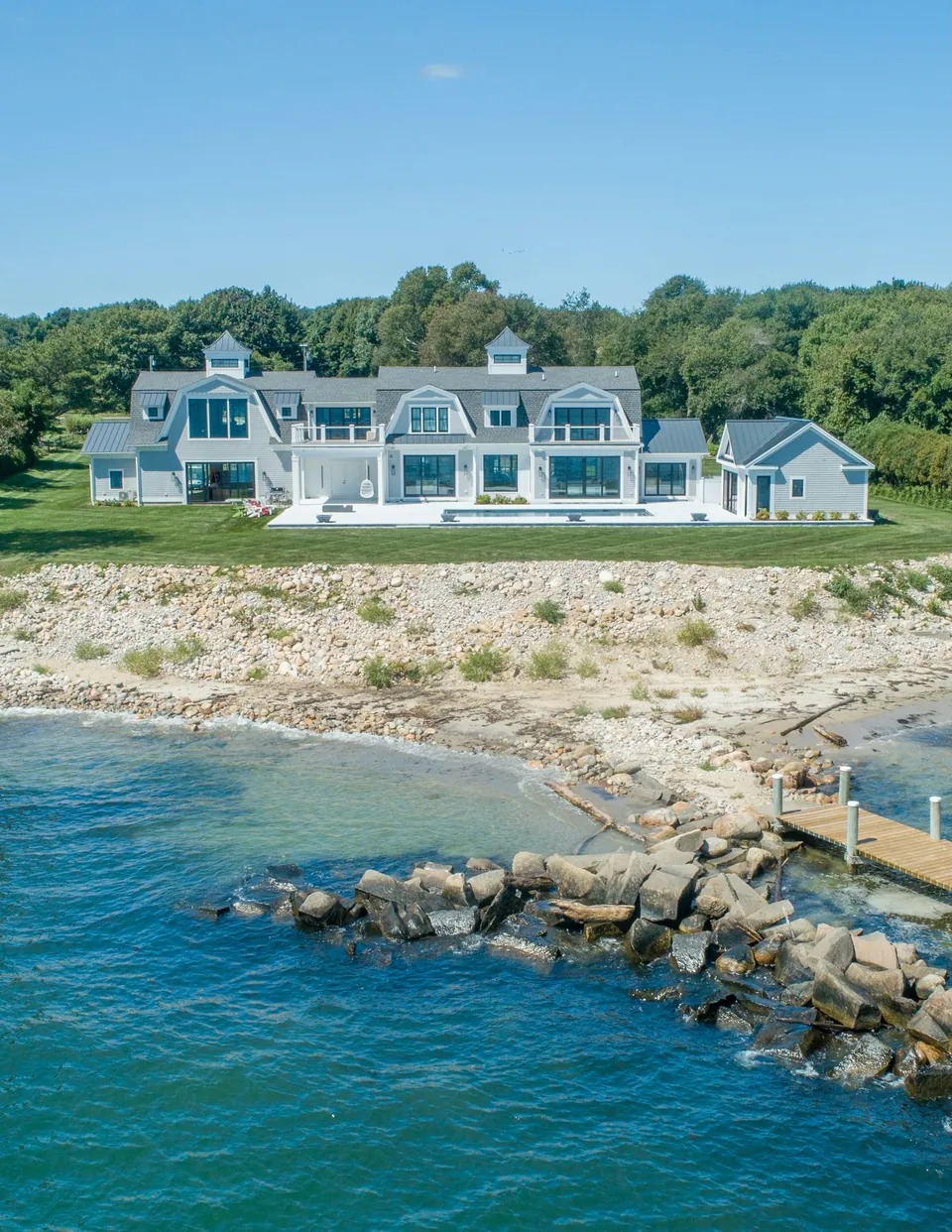 Coastal home with crisp white trim, gambrel roofs, a finished terrace and maintained lawn